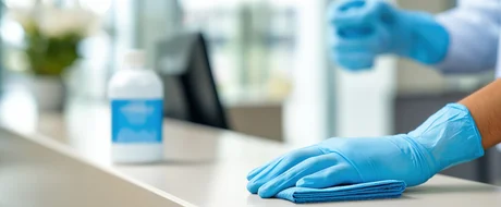 PEG - Gebäudereinigung im Gesundheitswesen Reinigungskraft mit Handschuhen reinigt eine Oberfläche mit einem Tuch
