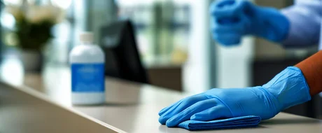 Reinigungskraft mit Handschuhen reinigt eine Oberfläche mit einem Tuch