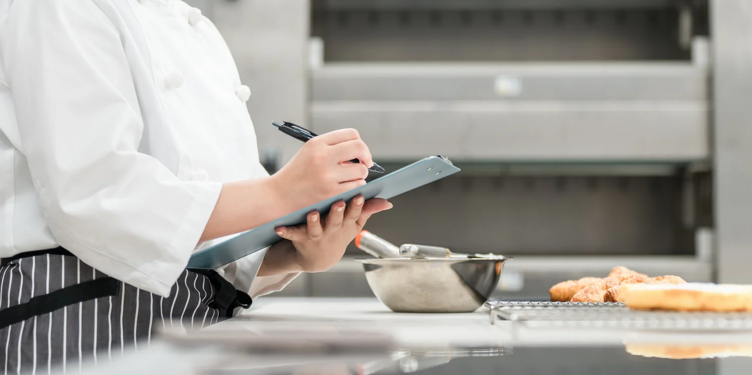 PEG - Speisenversorgung in der Gemeinschaftsverpflegung Mitarbeiterin mit Haarnetz bei der Portionierung von Speisen in einer Großküche