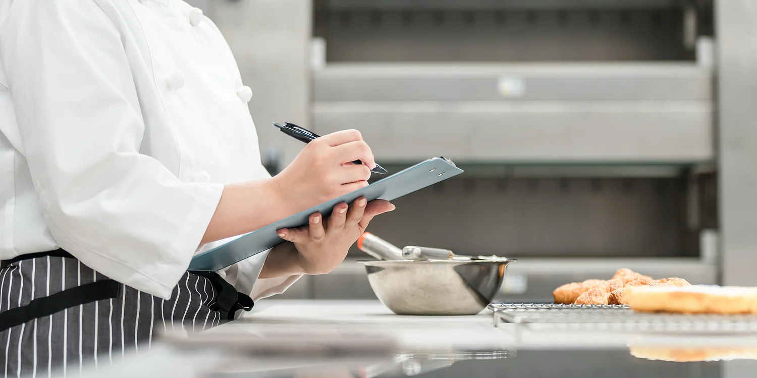 PEG - Speisenversorgung in der Gemeinschaftsverpflegung Mitarbeiterin mit Haarnetz bei der Portionierung von Speisen in einer Großküche